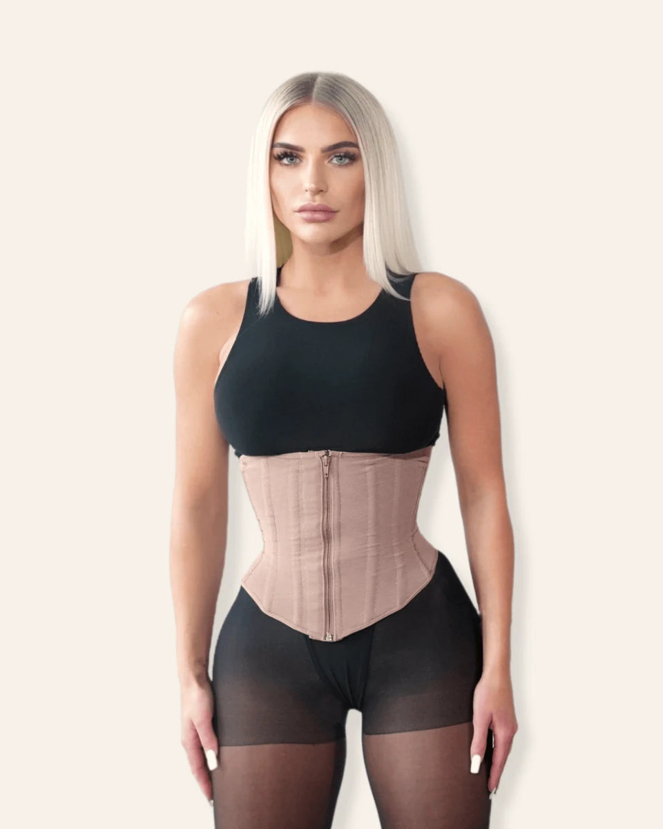 The Sculpt Waist Trainer worn in Sandstone over a black tank, front view, showing the curved front panel and hook-and-eye closure